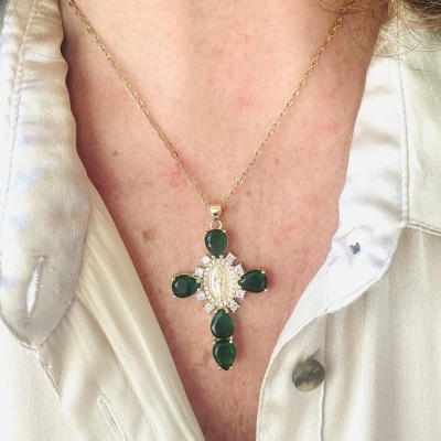 Colar com pendente em forma de cruz com pedras verdes e detalhes brancos usado com camisa branca