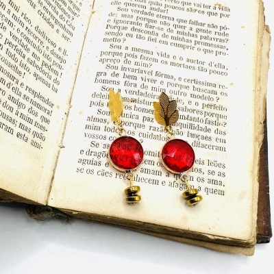 Brincos com pedra vermelha e pendente de folha dourada sobre livro antigo aberto