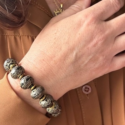 Pulseira com contas pretas e douradas em pulso de pessoa com camisa castanha