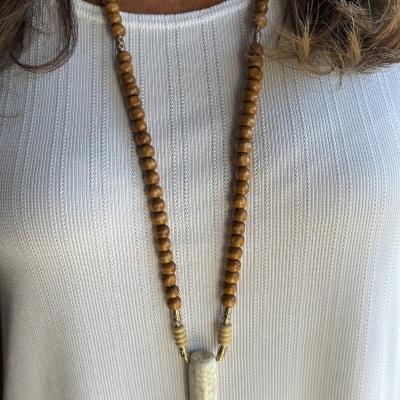 Colar de contas de madeira castanha com pendente claro em forma de dente sobre t-shirt branca texturada