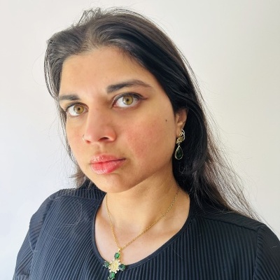 Mulher com camisa preta e joias douradas com pedras verdes