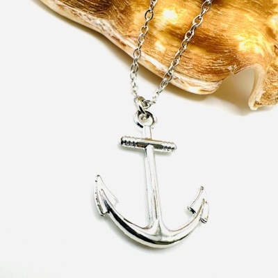 Colar com pendente de âncora prateada junto a uma concha