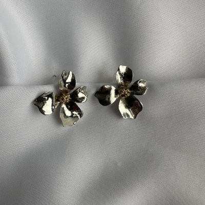 Brincos florais em metal prateado com detalhes dourados sobre tecido branco