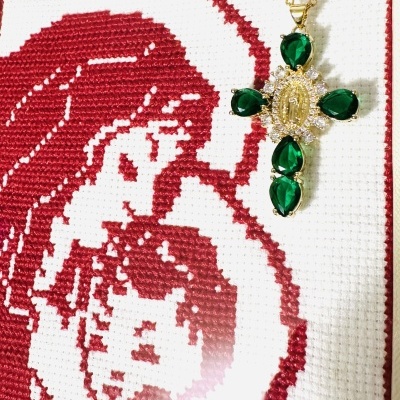 Colar com pendente em cruz e pedras verdes sobre pano bordado