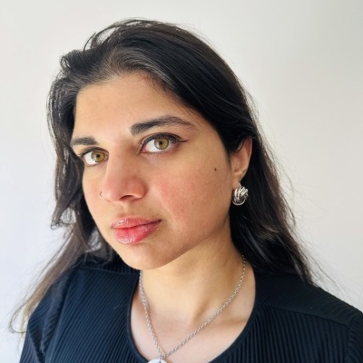 Mulher com colar de pendente redondo e brincos prateados, vestindo camisa preta, fundo branco.