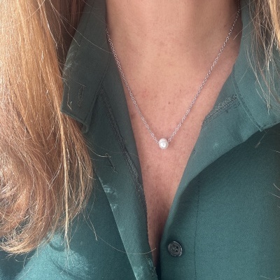 Colar com corrente prateada e pérola pendente sobre camisa verde escura com gola