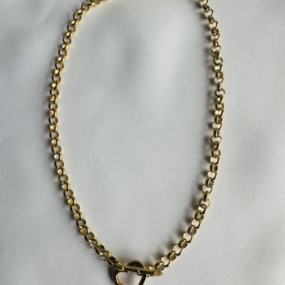 Colar dourado com fecho coração sobre tecido branco