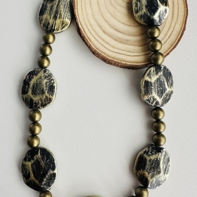 Colar com contas pretas e bege e esferas douradas sobre fundo branco e disco de madeira
