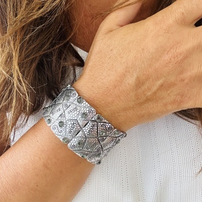 Pulseira larga prateada com padrão geométrico no pulso de pessoa com camisola branca