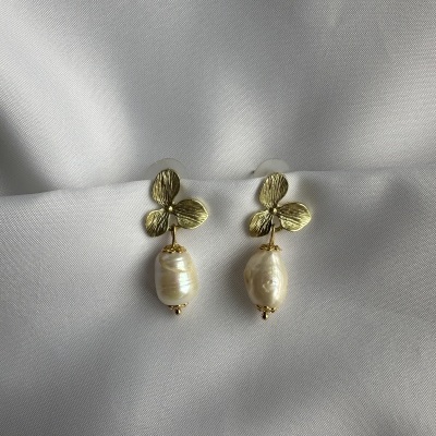 Brincos dourados com pérolas sobre tecido branco acetinado