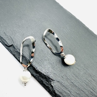 Brincos prateados com pérolas brancas sobre ardósia cinzenta