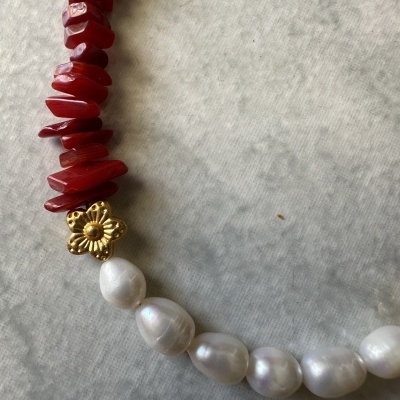 Colar com pérolas brancas, pedras vermelhas e flor dourada sobre superfície cinza