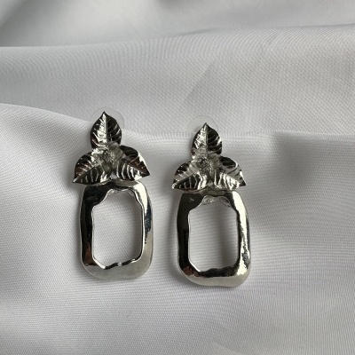 Brincos prateados com folhas e forma retangular sobre tecido branco