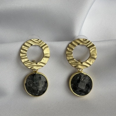 Par de brincos dourados com pedras escuras sobre tecido branco