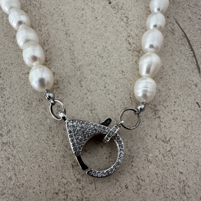 Colar de pérolas com fecho prateado brilhante em superfície de pedra.