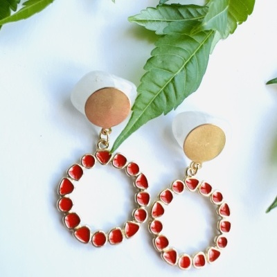 Brincos dourados com pedras vermelhas e fundo branco com folhas verdes