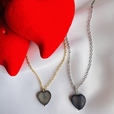 Colares com pendentes de coração escuro em correntes dourada e prateada sobre tecido branco com corações vermelhos