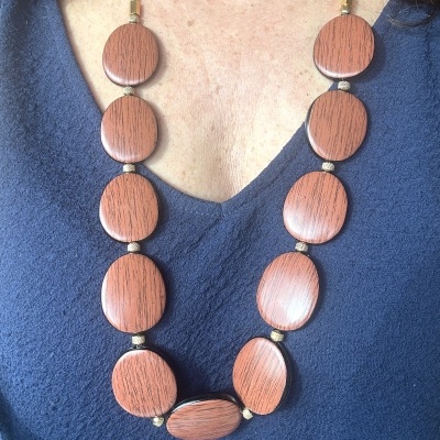 Colar de grandes peças ovais de madeira castanha com esferas douradas sobre blusa azul