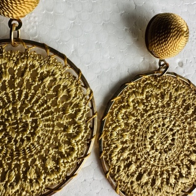 Brincos redondos dourados com superfície texturada e padrão tecido, sobre fundo branco texturizado
