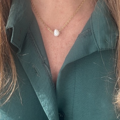 Colar dourado com pérola branca ao centro numa camisa verde escura