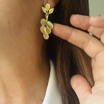 Brinco dourado com folhas e frutos pendentes usado por mulher com cabelo castanho