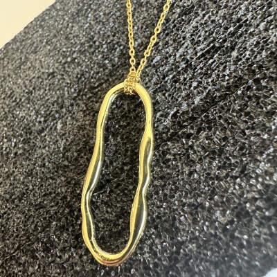 Colar dourado com pingente irregular sobre fundo preto texturado