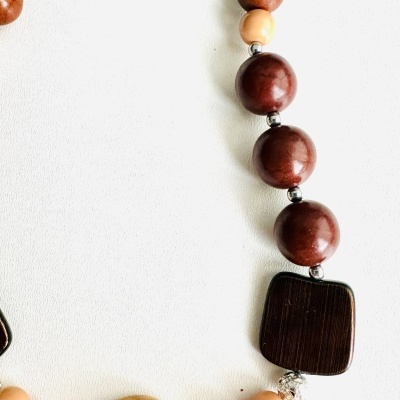 Colar com contas de madeira castanhas e nude e uma conta preta circular com padrão, em fundo branco.