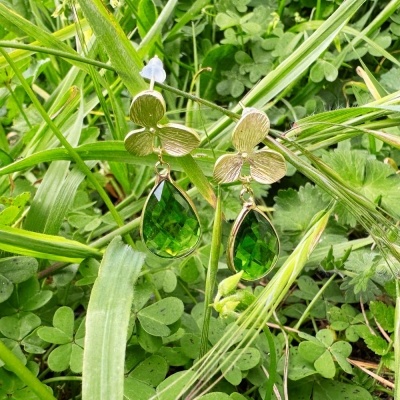 Brincos pendentes verdes com contas de trevo douradas sobre vegetação verde