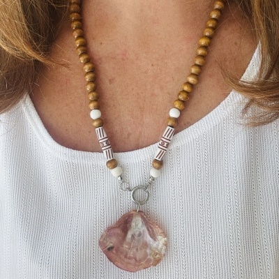 Colar de contas de madeira com pendente de pedra rosa sobre blusa branca texturada