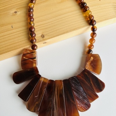 Colar com contas âmbar e placas castanhas em leque sobre tábua de madeira clara