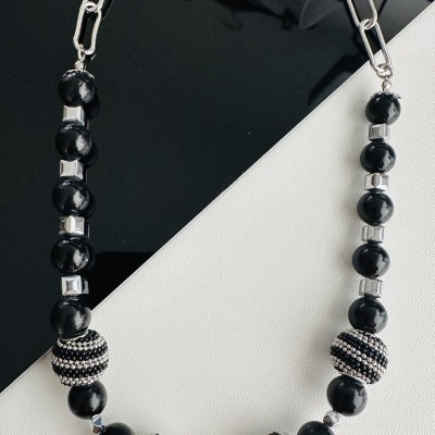 Colar com contas pretas, contas decoradas com cristais e elos prateados sobre fundo preto e branco