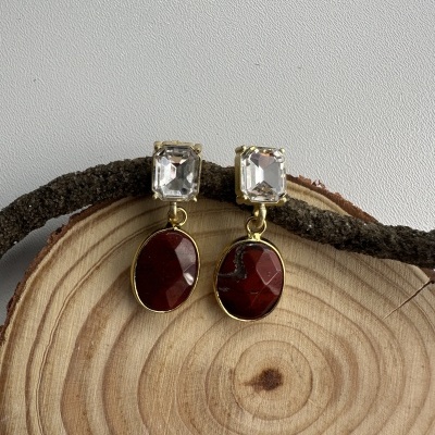 Brincos com pedras transparente e vermelha sobre madeira clara com ramo seco