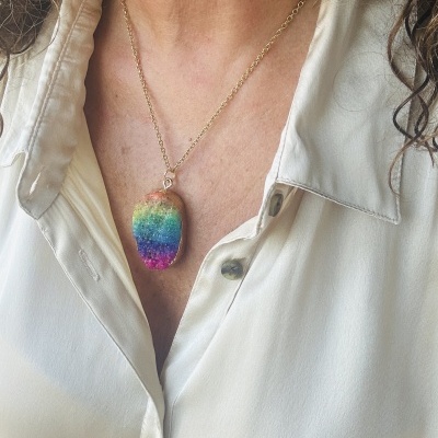 Colar com pendente oval colorido em arco-íris com corrente dourada numa camisa branca