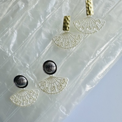 Dois pares de brincos com design de leque, base dourada texturada e base preta lisa, sobre plástico transparente