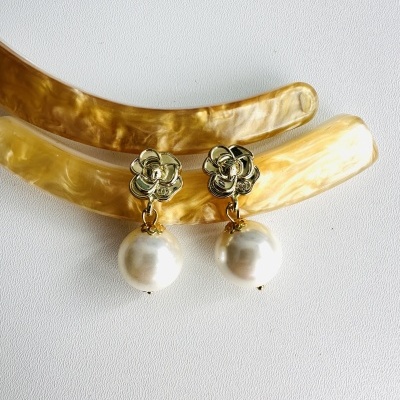 Brincos dourados com pérolas penduradas sobre superfície branca e objetos amarelo-dourados.