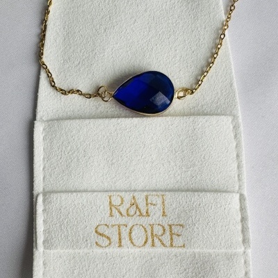 Colar dourado com pedra azul em porta-joias branco com 'RAFI STORE'