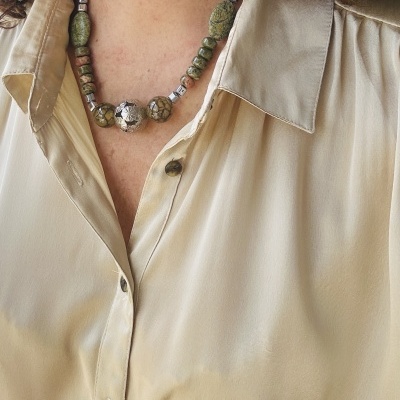 Colar com contas em tons verdes e cinza sobre camisa bege clara