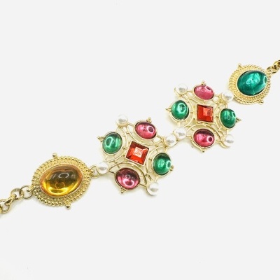 Pulseira dourada com pedras coloridas e pérolas sobre fundo branco