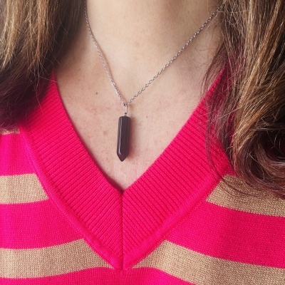 Colar com pingente preto em forma de prisma hexagonal sobre camisola riscada em bege e rosa-fúcsia