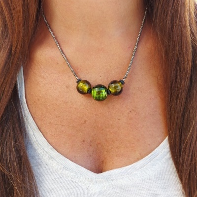 Colar com contas verdes e amarelas em corrente metálica, usado por pessoa com camiseta branca