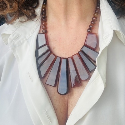 Colar com pendentes castanhos brilhantes e contas esferas usados sobre camisa branca