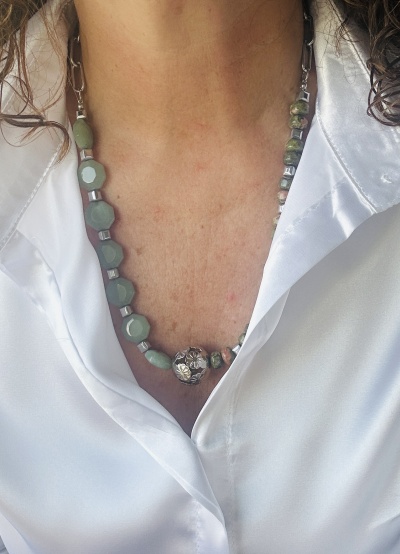 Colar de pedras verdes com pendente metálico sobre camisa branca acetinada