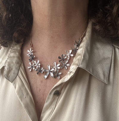 Colar de flores prateadas em pescoço com camisa bege