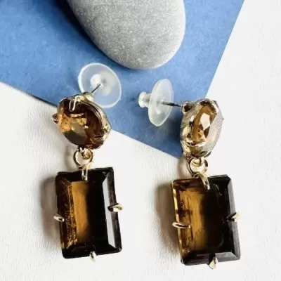 Brincos com pedras castanho-âmbar facetadas em fundo azul e branco