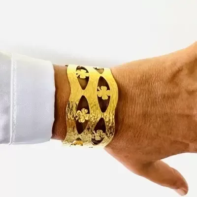 Pulseira larga dourada com padrão recortado em pulso com camisa branca