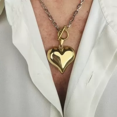 Colar corrente prateada com pendente coração dourado sobre camisa branca