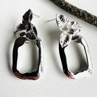 Brincos prateados com folhas e estrutura oval sobre superfície branca