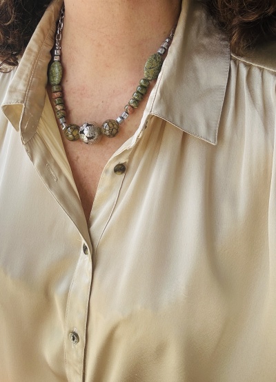 Colar com contas em tons verdes e cinza sobre camisa bege clara