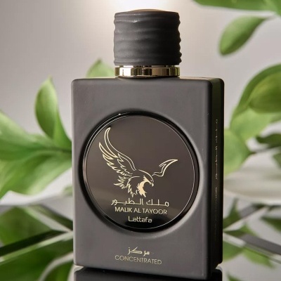 Frasco preto de perfume Malik Al Tayoor Lattafa com tampa preta e detalhes dourados, sobre superfície refletora e fundo de plantas verdes.
