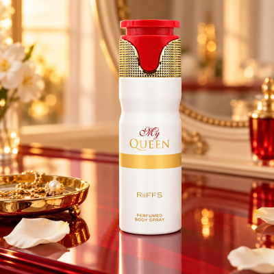 Frasco de spray corporal perfumado branco com detalhes dourados e tampa vermelha numa mesa vermelha com joalharia e pétalas.